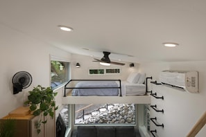 A compact room with a bunk bed, a ceiling fan, a window with a view, and a wall-mounted air conditioning unit.