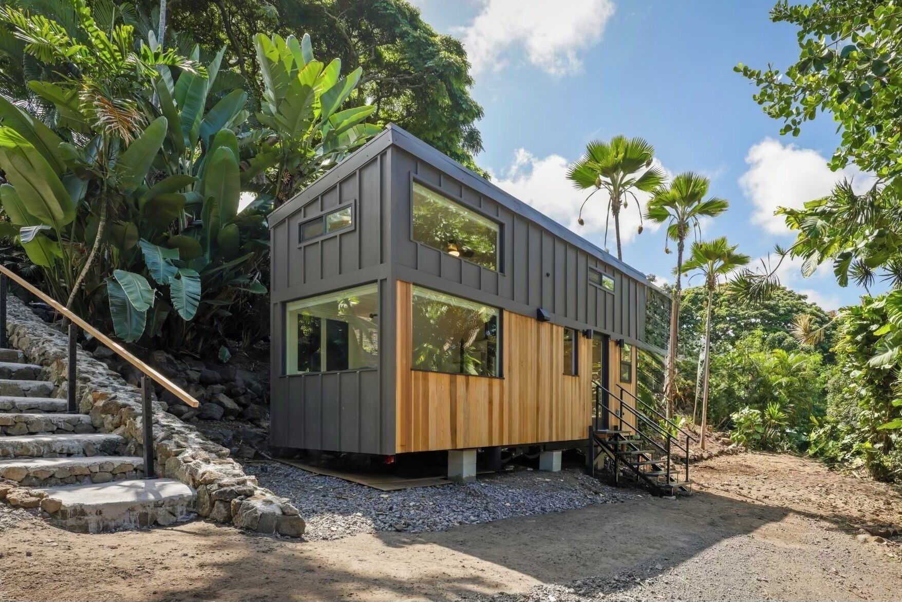 Une maison moderne à deux étages, dotée de grandes fenêtres, d’un revêtement extérieur en bois et d’un escalier menant à l’étage supérieur.