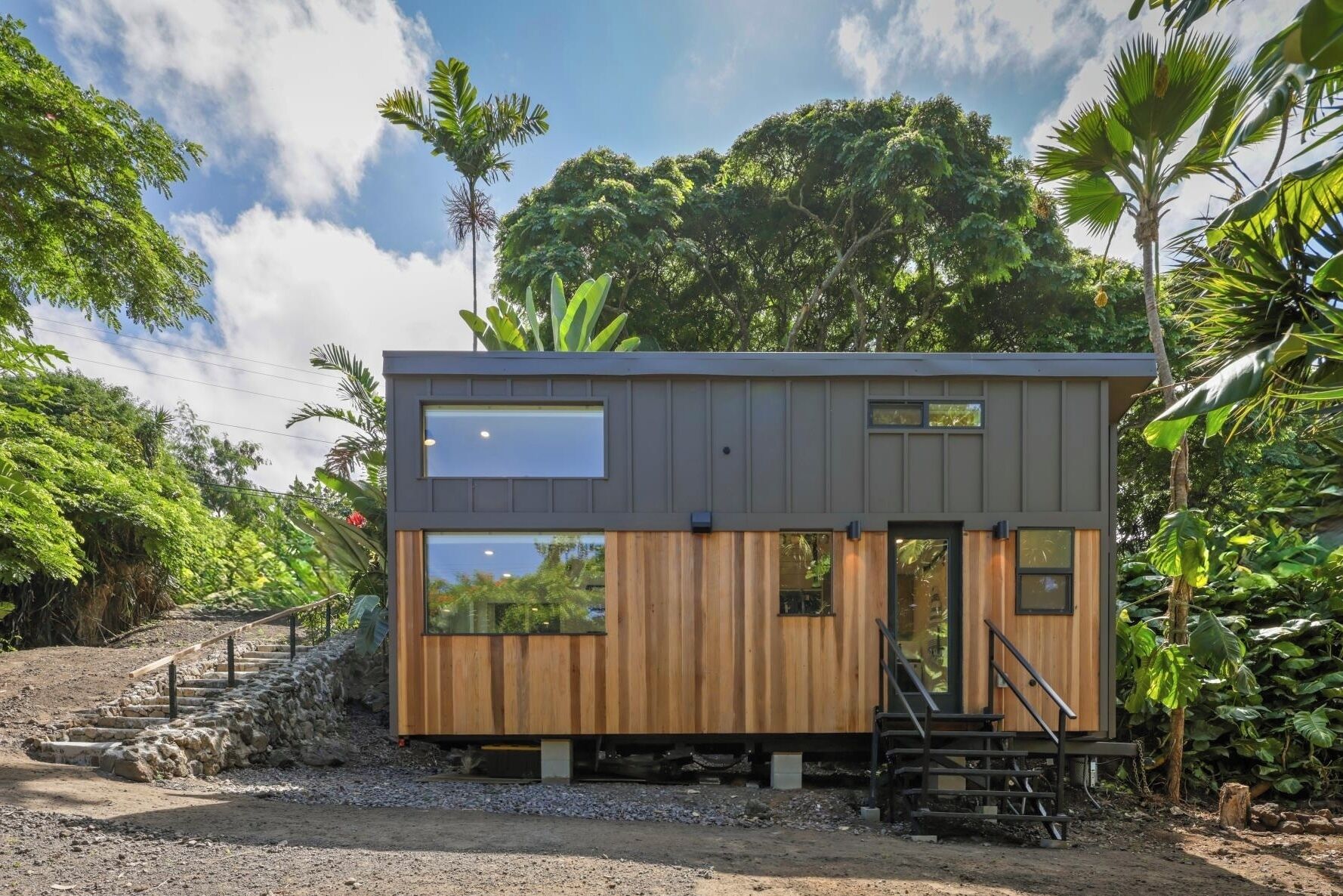 A modern, two-story cabin with a wooden facade and large windows, surrounded by lush greenery.