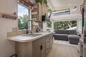 A modern kitchen with a built-in island, a dining area with a grey sofa, and a view of the outdoors.