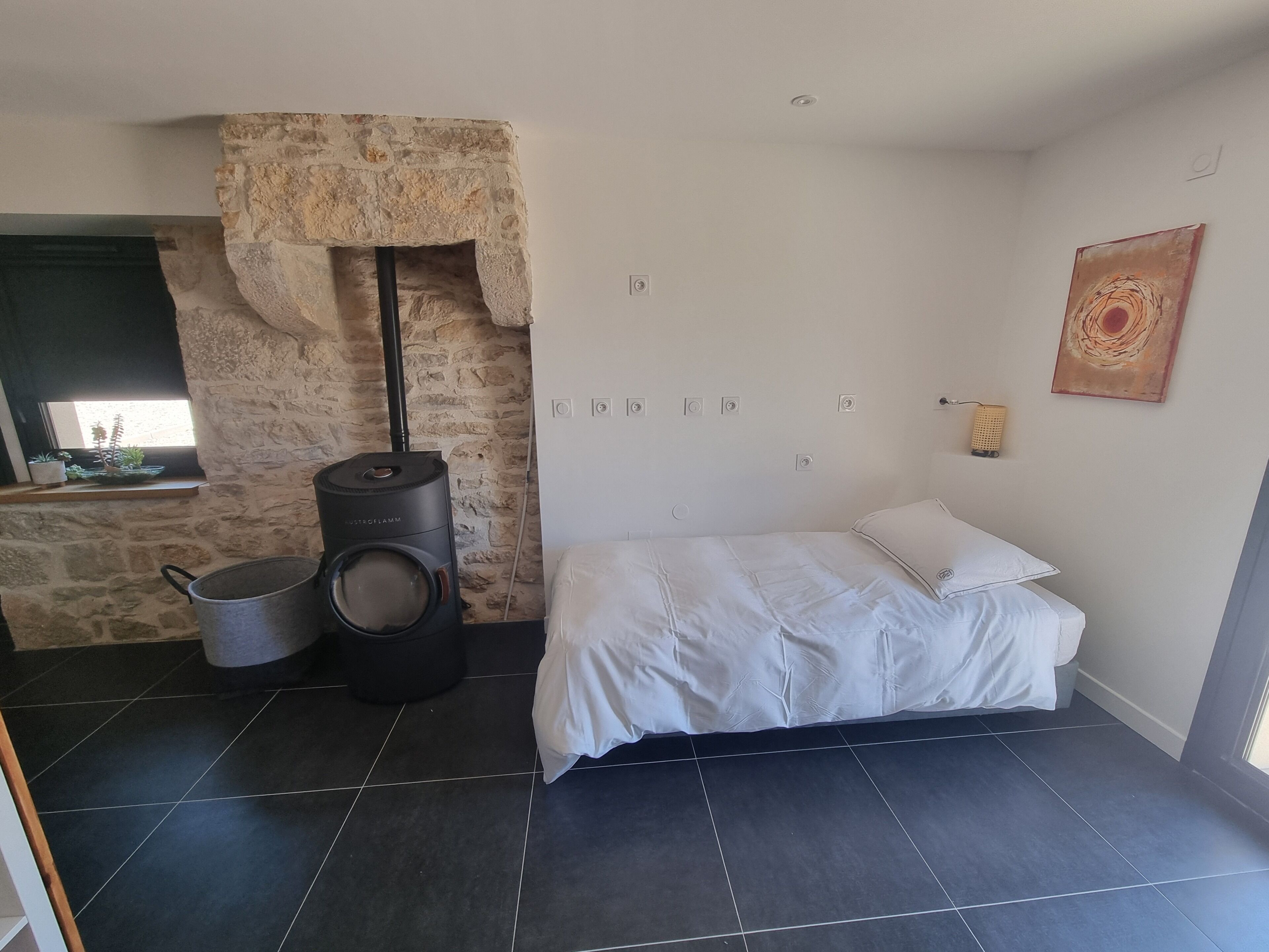 Un dormitorio con pared de piedra, cama, calentador y ventana.