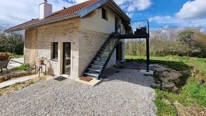 Uma casa de pedra com telhado de cerâmica, uma escadaria que dá para uma varanda e um caminho de acesso de brita.