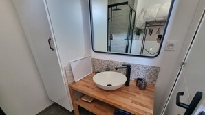 Uma casa de banho com toucador de madeira, lavatório suspenso branco, torneira preta e espelho sobre o lavatório.