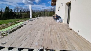 Um deck de madeira com vista para o campo, um edifício branco com uma porta e um céu claro.