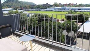 Un balcon avec une table et des chaises, donnant sur un terrain de sport et des immeubles.