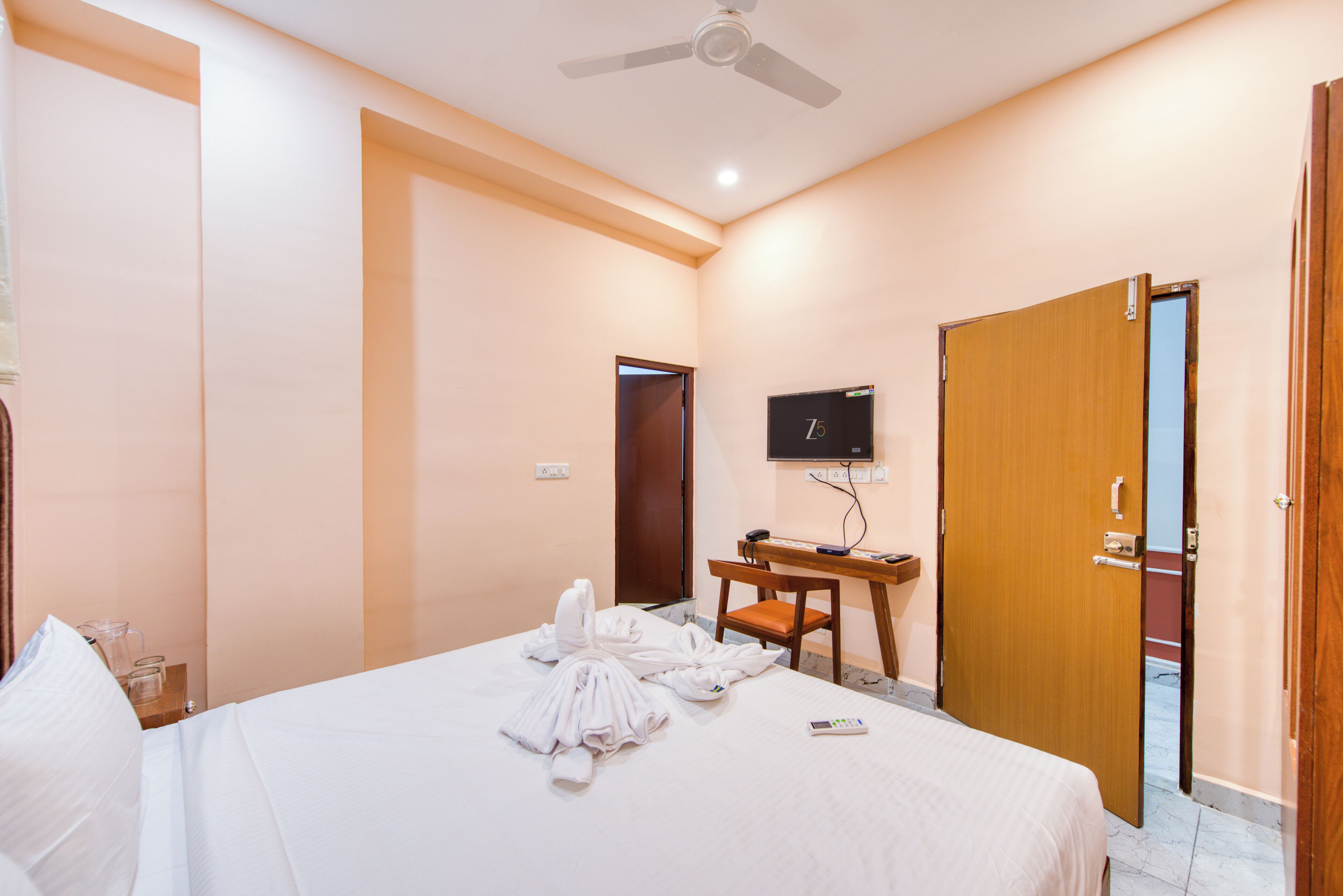 A hotel room with a bed, a desk, a television, and a door.