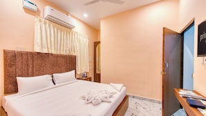 Habitación de hotel con cama, mesita de noche, unidad de aire acondicionado, ventilador de techo, espejo de baño y puerta.