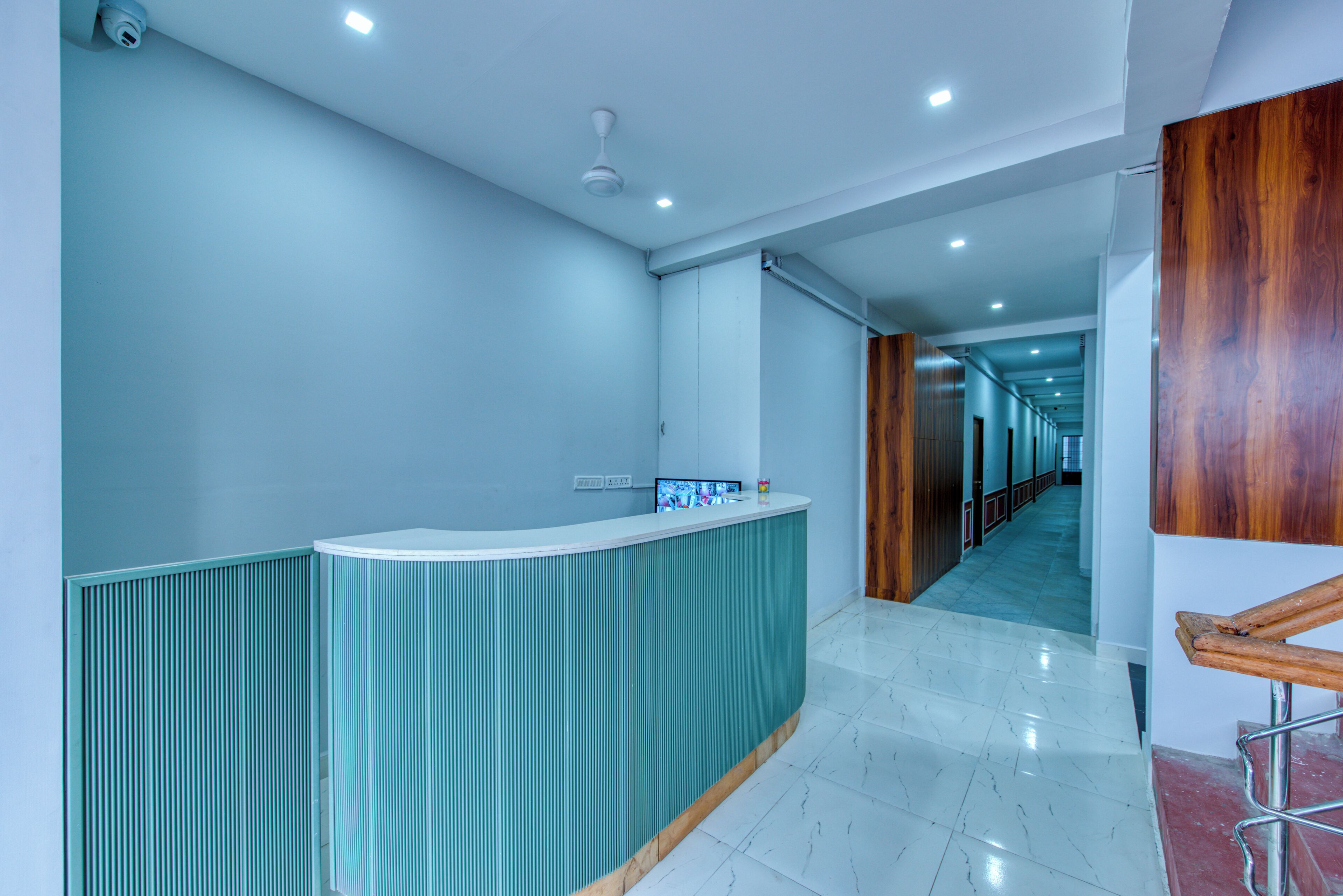 A modern reception area with a curved counter, a ceiling fan, and a hallway leading to a wooden door.