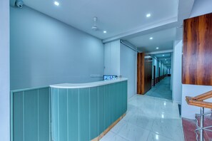 Un área de recepción moderna con un mostrador curvo, un ventilador de techo y un pasillo que conduce a una puerta de madera.