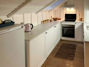 Eine kompakte Küche mit weißen Schränken, einem eingebauten Backofen, einer Kaffeemaschine und einer Fruchtschale auf der Arbeitsplatte.