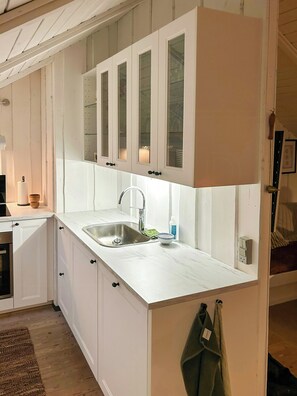 Une cuisine avec des meubles blancs, un évier en acier inoxydable et un plancher en bois.