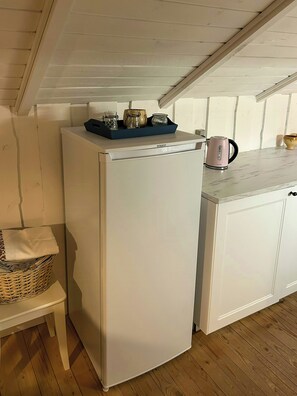 Eine kleine Küche mit einem weißen Kühlschrank, einer Holzbank und einem Korbwannenkorb.