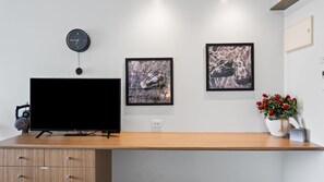 A modern room with a flat-screen TV, a clock, and two framed pictures on the wall.