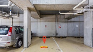 Un parking avec des piliers en béton, une voiture garée au premier plan et des panneaux d’avertissement sur les murs.