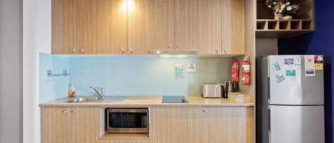 A compact kitchen with wooden cabinets, a stainless steel sink, a microwave, a toaster, and a refrigerator.