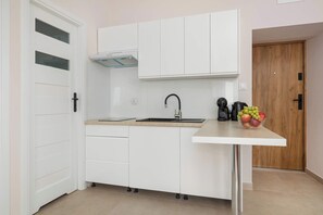 Une cuisine moderne avec des meubles blancs, un évier en acier inoxydable et un panier de fruits posé sur le plan de travail.