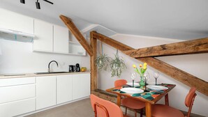 Cozinha moderna com armários brancos, teto de madeira e área de jantar com mesa posta para dois.