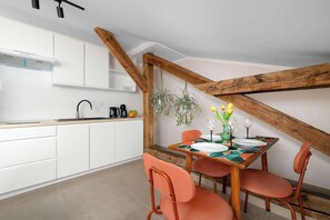 Eine moderne Küche mit weißen Schränken, einer Holzbalkendecke und einer Essecke mit Tisch für zwei Personen.