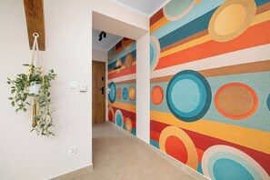 Ein Flur mit einem farbenfrohen, abstrakten Wandgemälde, einer hängenden Pflanze und einem Holzbalken an der Decke.