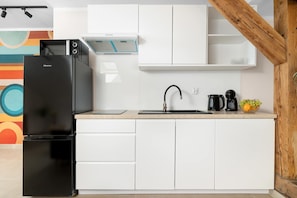 Eine kompakte Küche mit einem schwarzen Kühlschrank, weißen Schränken, einer Spüle und einer Kaffeemaschine.
