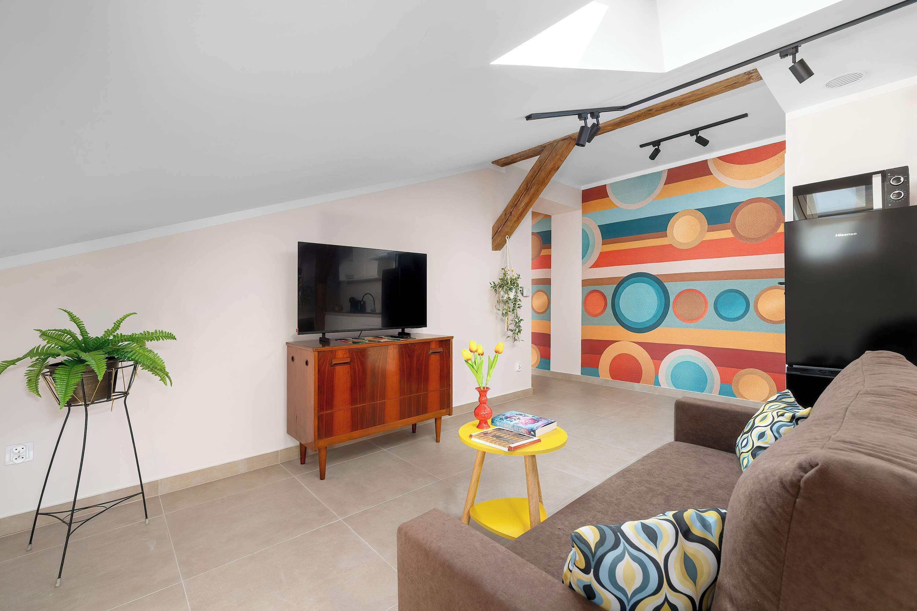 A modern living room with a TV, wooden cabinet, sofa, and colorful wall art.