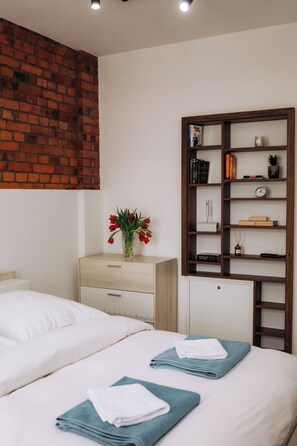 A hotel room with a brick wall, a wooden bookshelf, a desk, and a bed with towels. - Vrbo Property (Reichenbach im Vogtland)