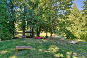 A grassy outdoor area with a wooden structure, picnic tables, and a wooden board game. - Luxe Home & Glamping w/ Pond in Oregon City! (Oregon City)