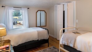 A room with two beds, a window with curtains, a mirror, and a bedside table with books. - Luxe Home & Glamping w/ Pond in Oregon City! (Oregon City)