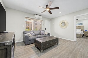 Un salon moderne avec un canapé gris, une table basse en bois et un ventilateur de plafond.
