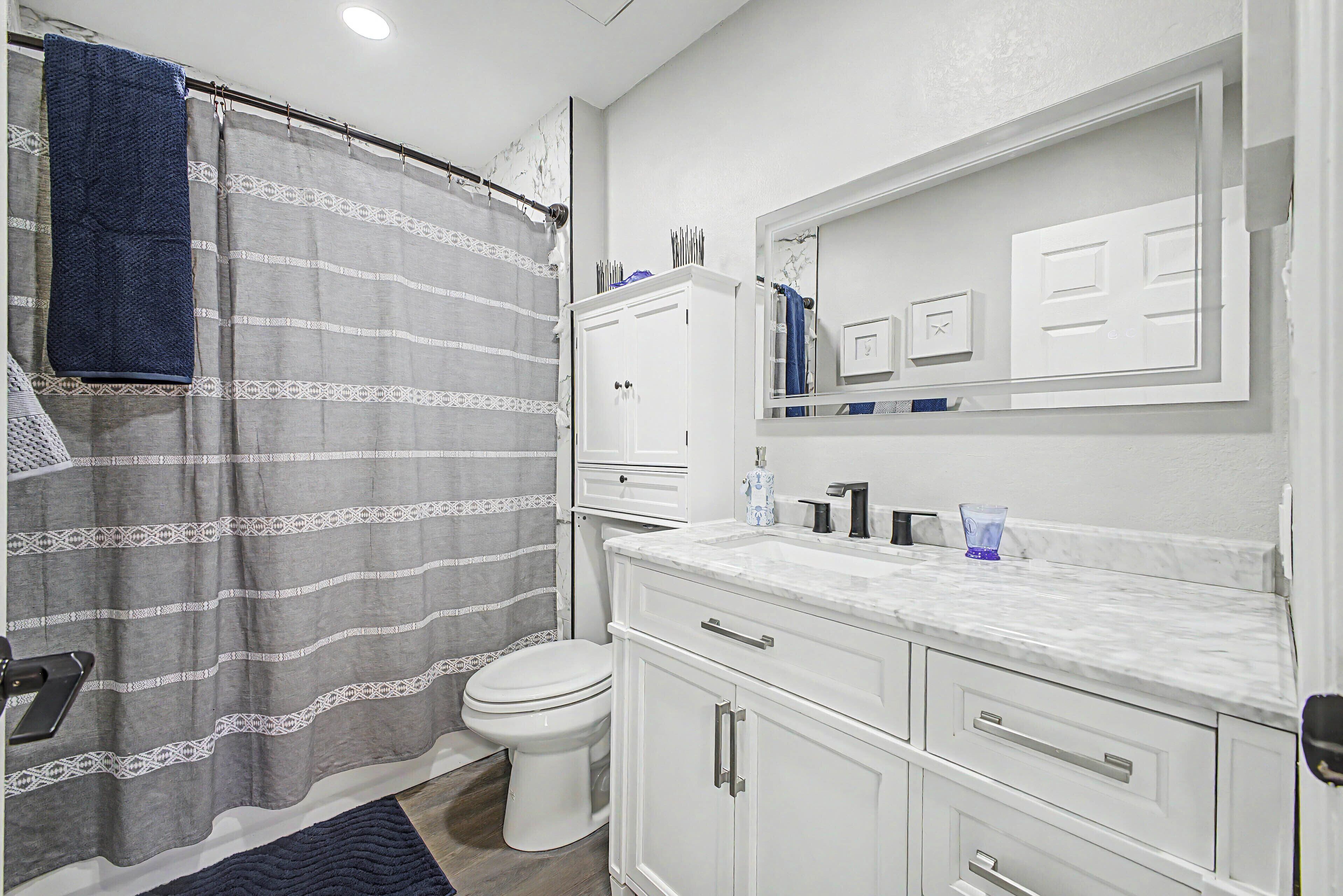 Une salle de bain équipée d’une douche avec rideau, de toilettes, d’un meuble-lavabo avec miroir et d’armoires.