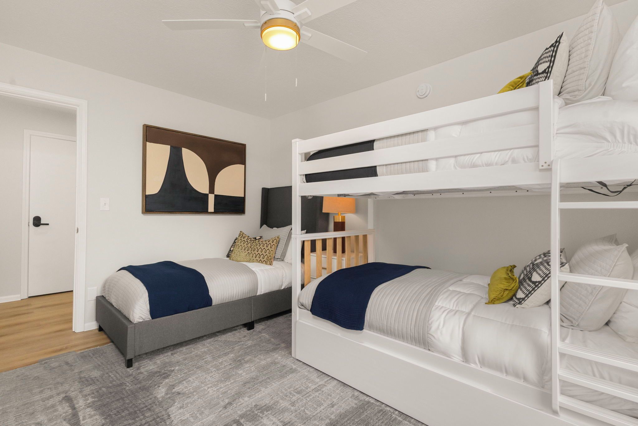 A bedroom with bunk beds, a ceiling fan, a painting, and a door.