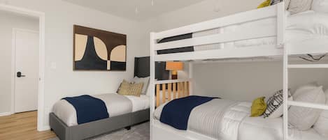 A bedroom with bunk beds, a ceiling fan, a painting, and a door.