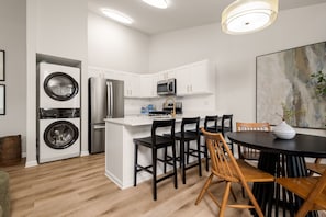 A modern kitchen with a central island, built-in appliances, and a dining area with wooden chairs. - Walk to ND Luxury 2BR/2BA Condo Balcony + Parking (South Bend)