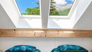 A room with two skylights, wooden beams, and two beds with peacock feather-patterned bedding.