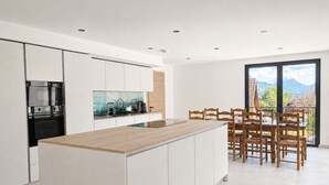 A modern kitchen with a central island, built-in appliances, and a dining area with wooden chairs.