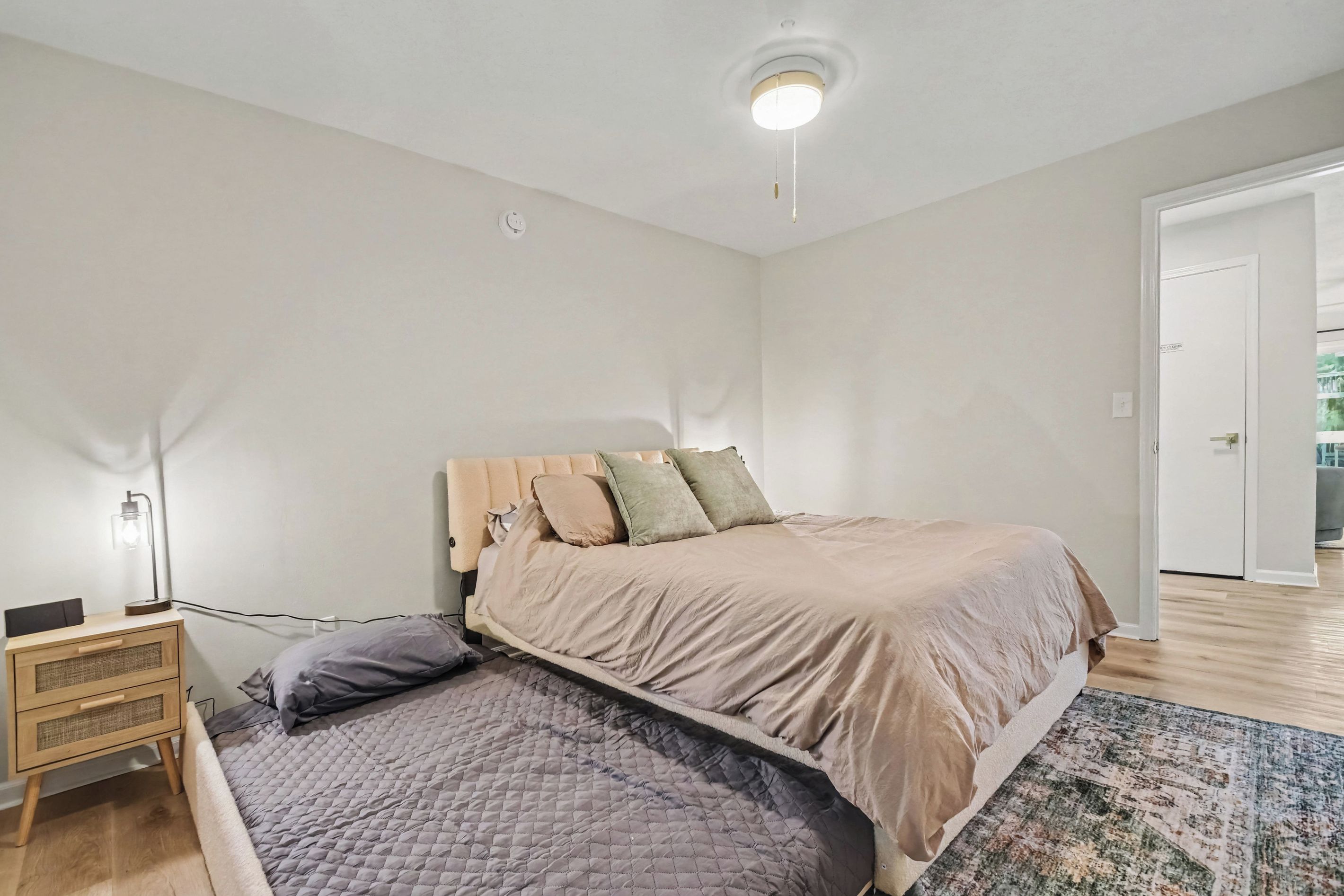 Un dormitorio con cama, mesita de noche, lámpara y una puerta que da a otra habitación.