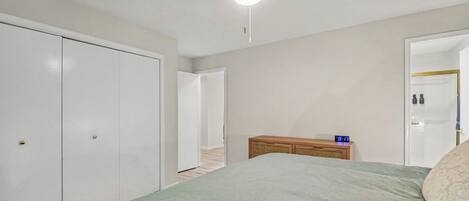 A bedroom with a bed, a bedside table with a clock, a wardrobe, and a door leading to another room.