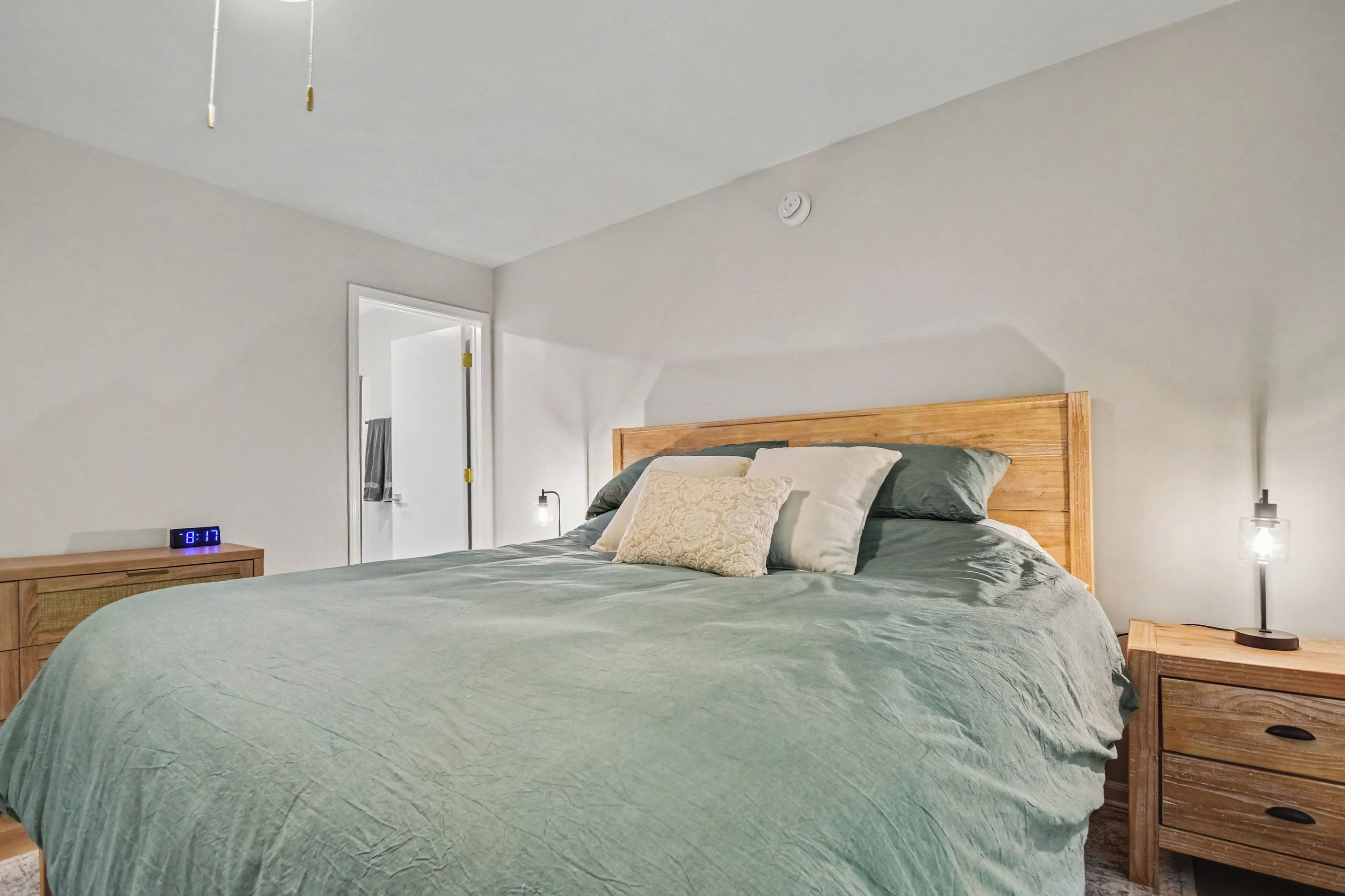 A bedroom with a bed, bedside tables, a nightstand, a wall clock, and a door.