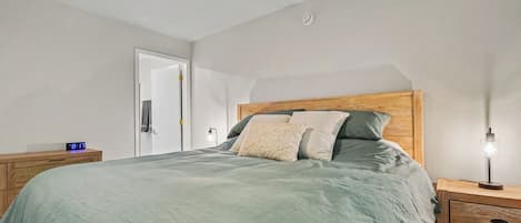 A bedroom with a bed, bedside tables, a nightstand, a wall clock, and a door.