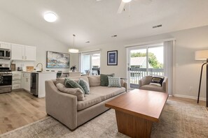 Una sala de estar moderna con sofá, mesa de centro y comedor, con cocina al fondo.