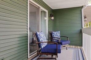 Une véranda avec deux fauteuils en osier et un coussin bleu, une porte-fenêtre coulissante et un mur extérieur vert.