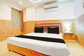 Una camera d'albergo con un letto, un condizionatore d'aria, un comodino e una finestra con tende.