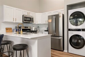 Una cocina moderna con armarios blancos, electrodomésticos de acero inoxidable y lavadora secadora integrada.