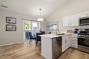 Une cuisine moderne avec des meubles blancs, des appareils en acier inoxydable et un coin repas doté de chaises bleues.