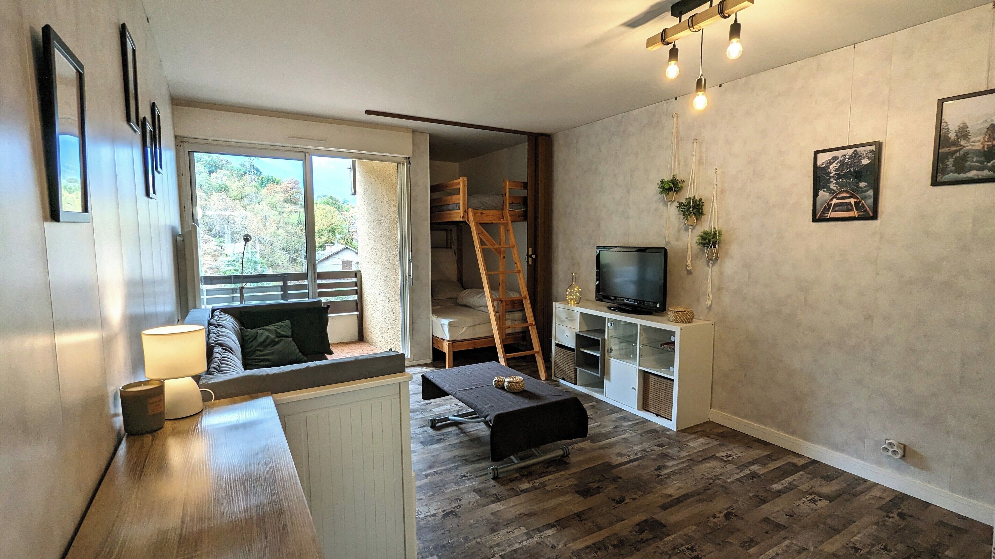 A compact living space with a bunk bed, a TV on a low shelf, and a window overlooking a garden.