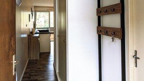 A hallway with a wooden bench, a shoe rack, and a door leading to a kitchen. - Studio le banga (Ax-les-Thermes)