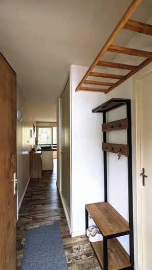Een gang met een houten bankje, een schoenenrek en een deur die naar een keuken leidt.