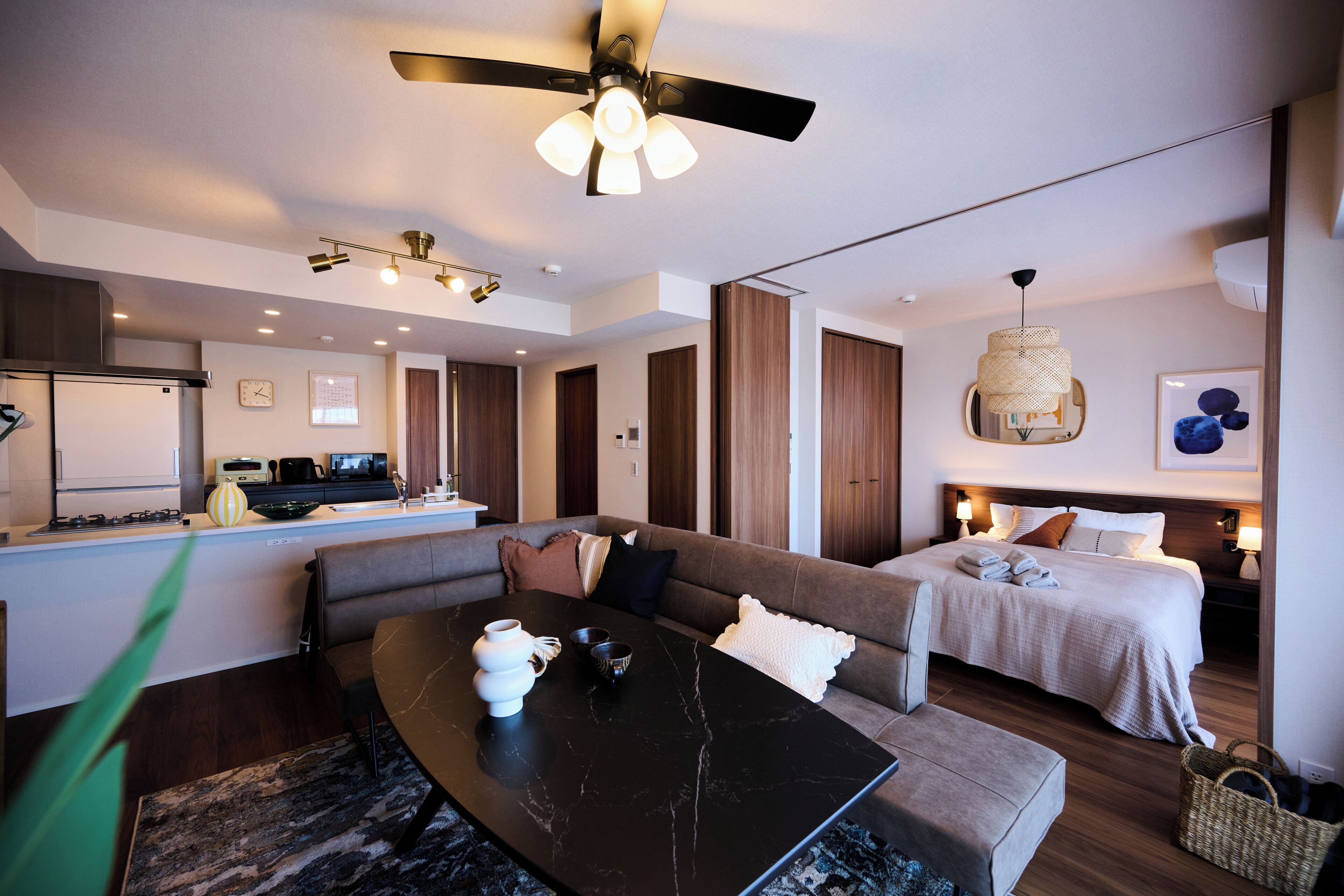 A modern hotel room with a dining area, a sofa, a bed, and a ceiling fan.