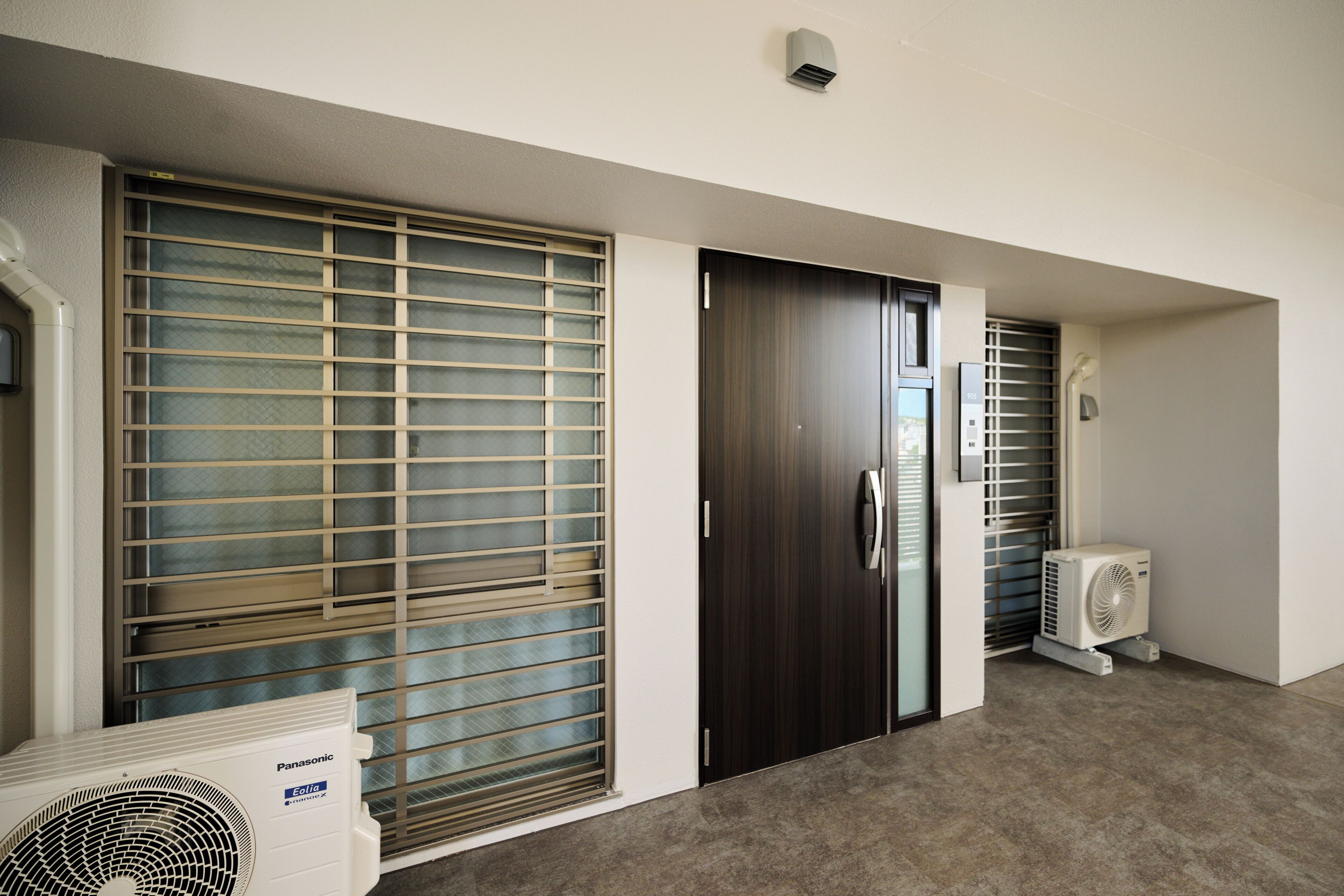 A hallway with a large window with blinds, a door, and a wall-mounted air conditioning unit.