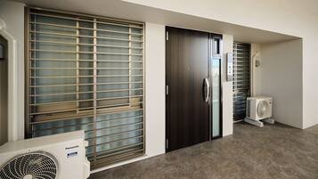 A hallway with a large window with blinds, a door, and a wall-mounted air conditioning unit.
